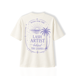 Back view of a white Thousand Lashes lash artist t-shirt displaying a purple "Lash Artist" graphic design with sunset and palm tree artwork.