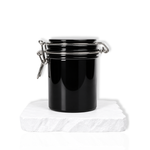 Black lash glue storage container with airtight lid displayed on a white stone surface.