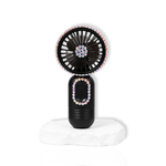 Black portable lash fan with rhinestone detailing displayed on a white stone surface.