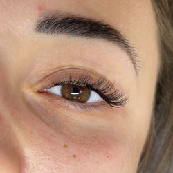 Close-up eye showing classic flat lash extensions with a soft natural look, dark matte black finish, and enhanced lash definition