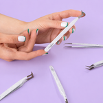 Hands holding a white marble-pattern eyelash extension tweezer with multiple lash tweezers displayed on a purple surface.