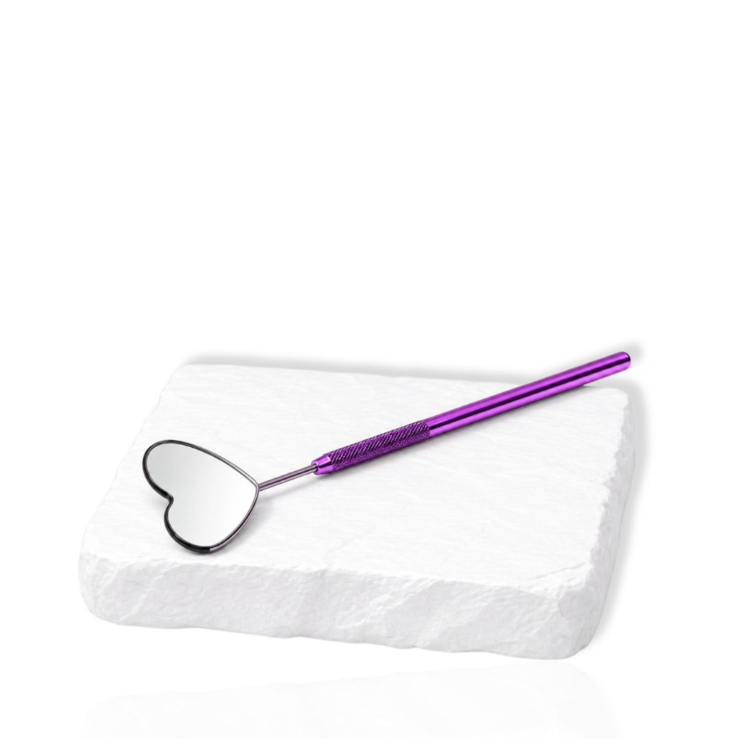 Purple eyelash extension mirror with a heart-shaped reflective head displayed on a white stone surface.