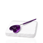 Purple heart-shaped eyelash extension mirror with a textured handle displayed on a white stone surface.