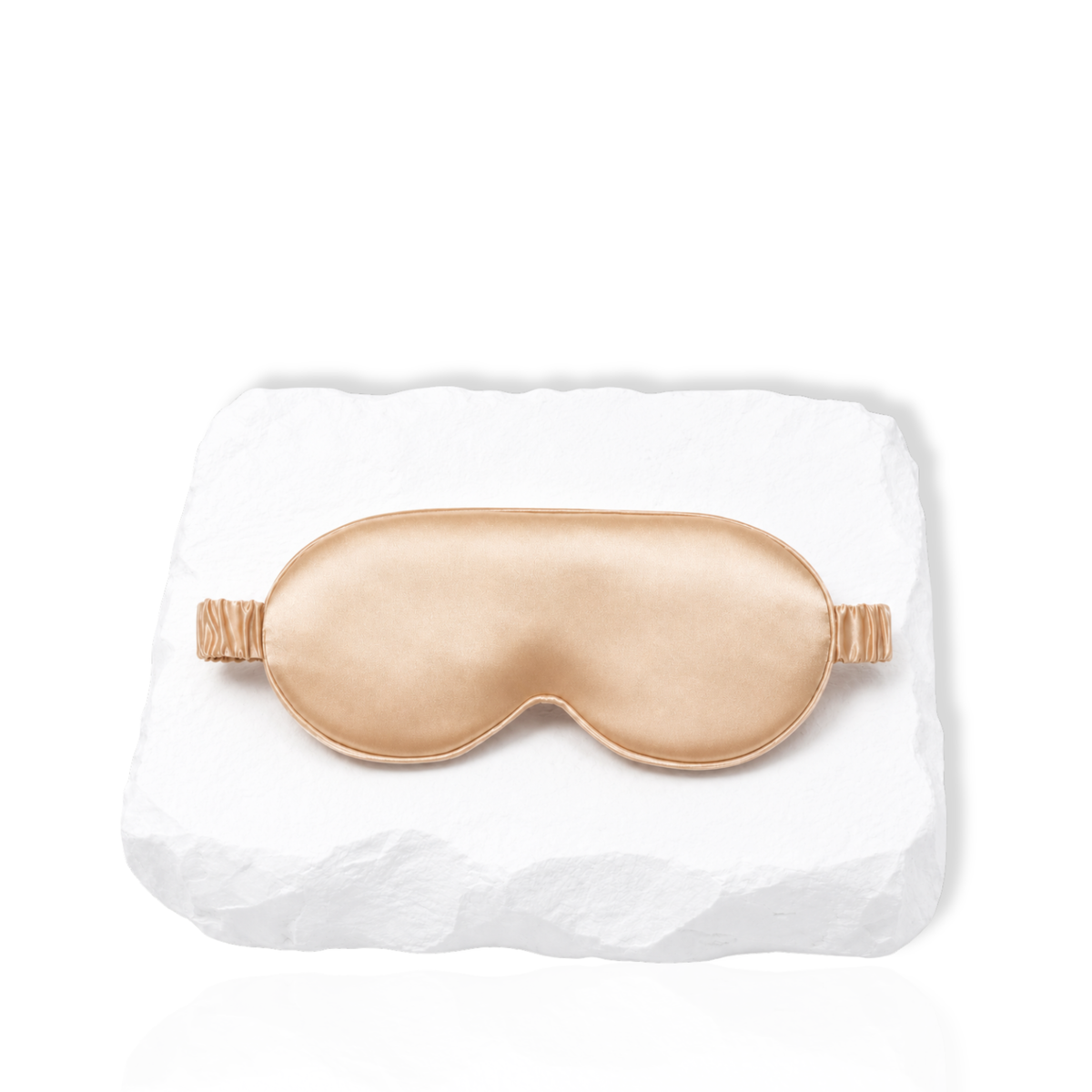 Silk lash mask with padded eye-shaped design and adjustable strap displayed on a white stone surface.