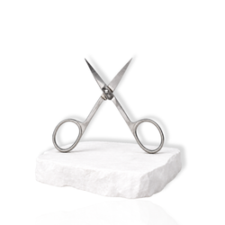 Stainless steel precision lash scissors with open blades displayed on a white stone surface against a white background.