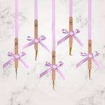 Thousand Lashes rose gold lash tweezers with gold tips displayed with purple ribbons on a marble background for professional eyelash extension tools.