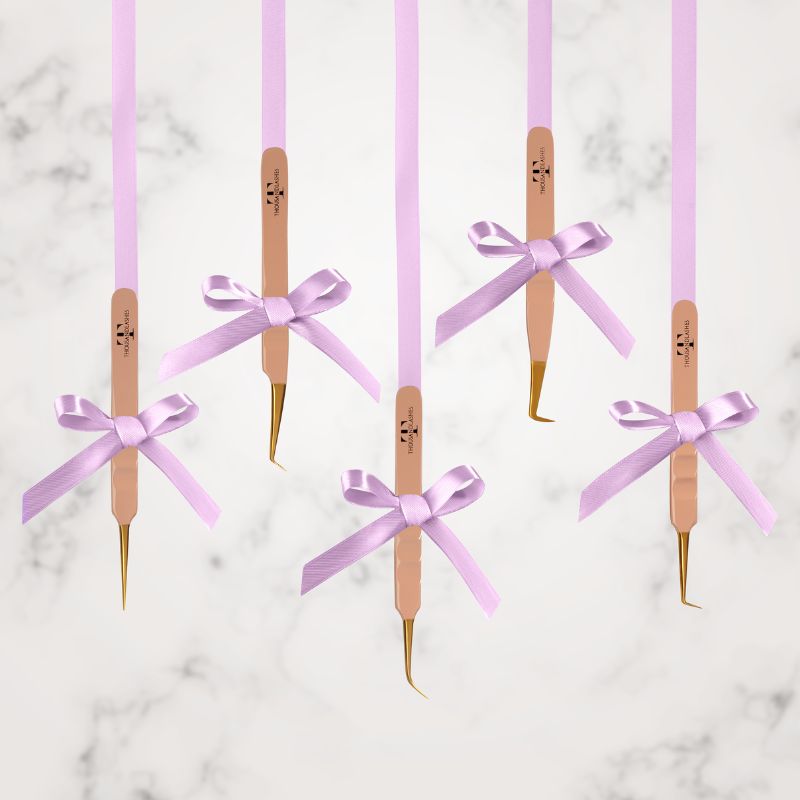 Thousand Lashes rose gold lash tweezers with gold tips displayed with purple ribbons on a marble background for professional eyelash extension tools.