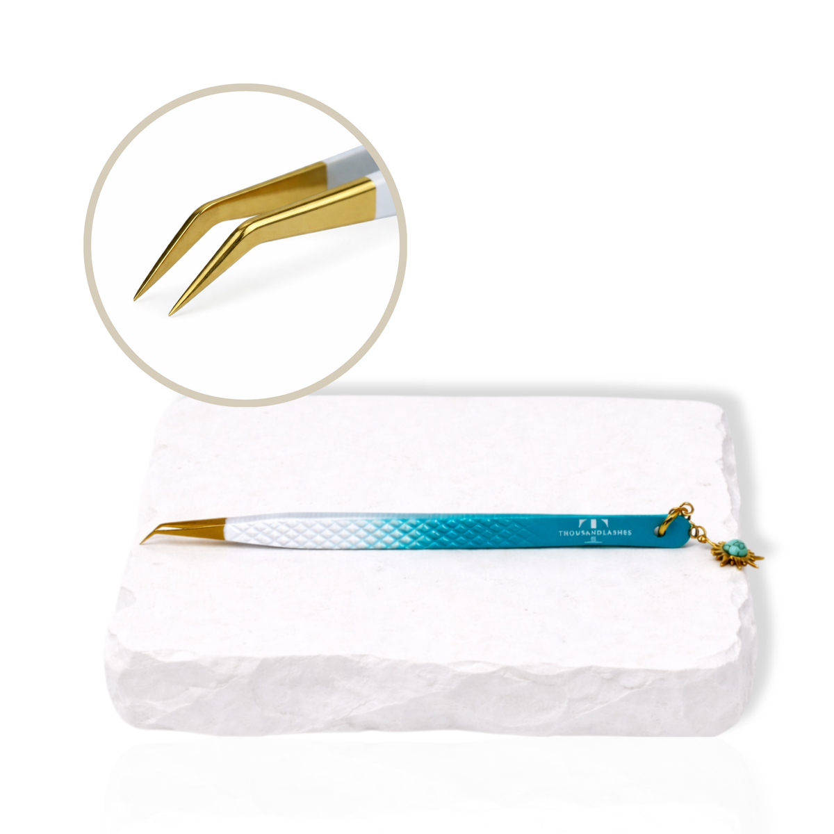 Thousandlashes Evil Eye precision lash tweezer with gold tip and sun charm on a white stone surface.