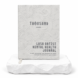 Thousandlashes Lash Artist Mental Health Journal with a gray wave-pattern cover displayed on a white stone surface.