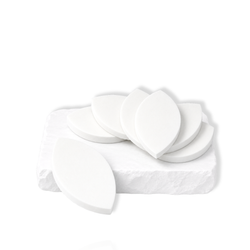 White leaf-shaped makeup sponges stacked and arranged on a white stone slab.
