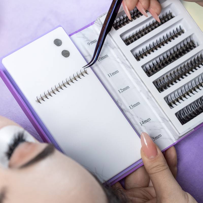 Lash artist using a Thousandlashes Noir Collection curved tweezer to pick up lash extensions from a tray.