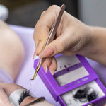 Lash artist using a rose gold curved tweezer to pick up eyelash extensions from a Thousand Lashes Pro Made Fans tray during a lash extension application.