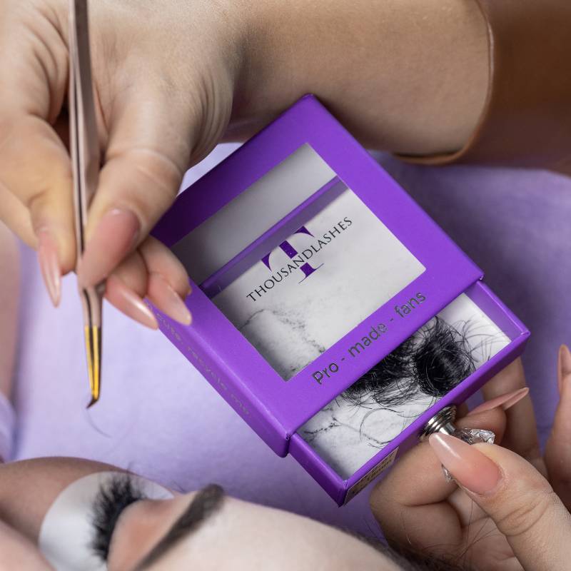 Lash artist using tweezers to create eyelash extensions with Thousand Lashes Pro Made Fans lash tray during a lash application treatment.